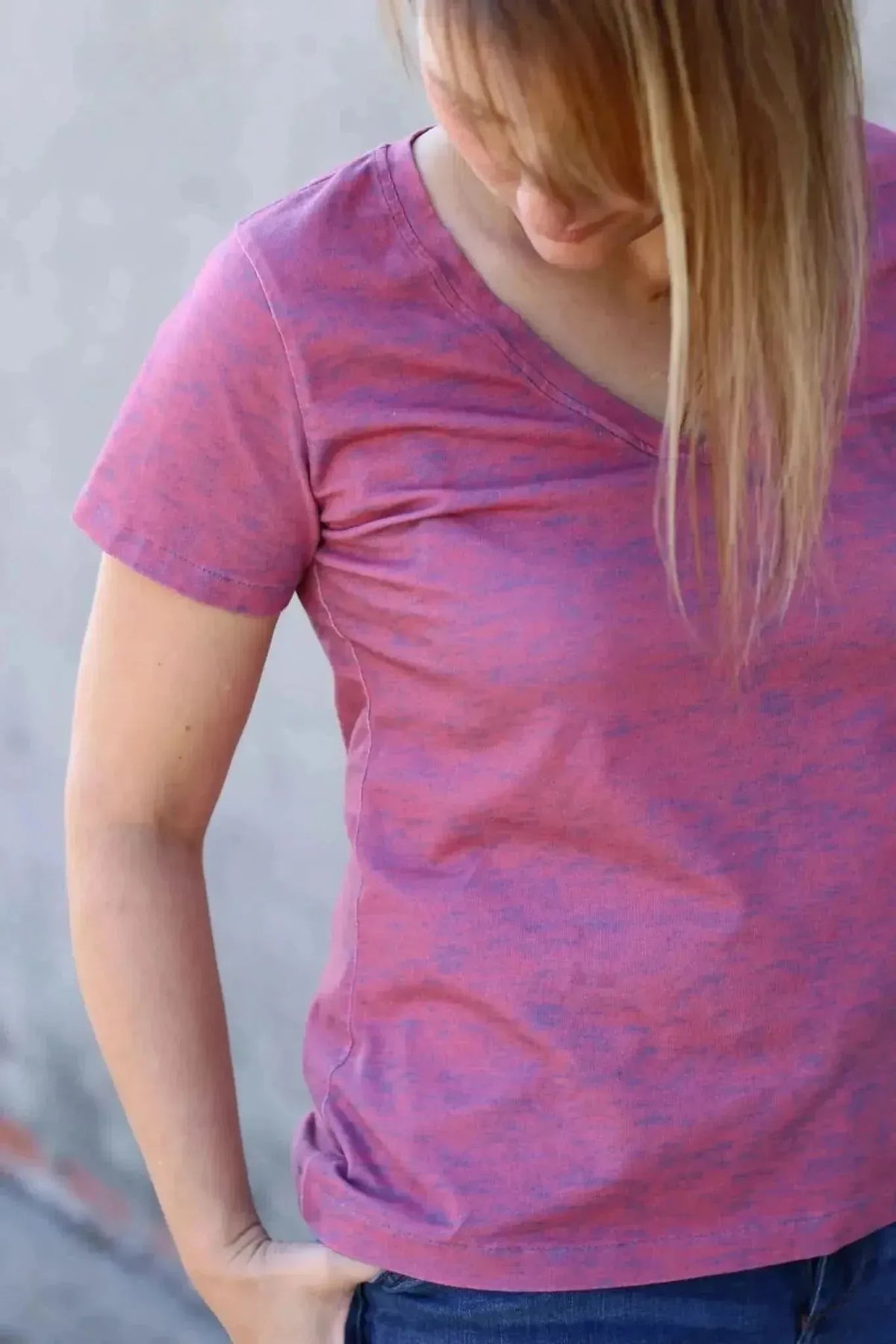 A woman wears a red heather v-neck t-shirt and blue jeans.