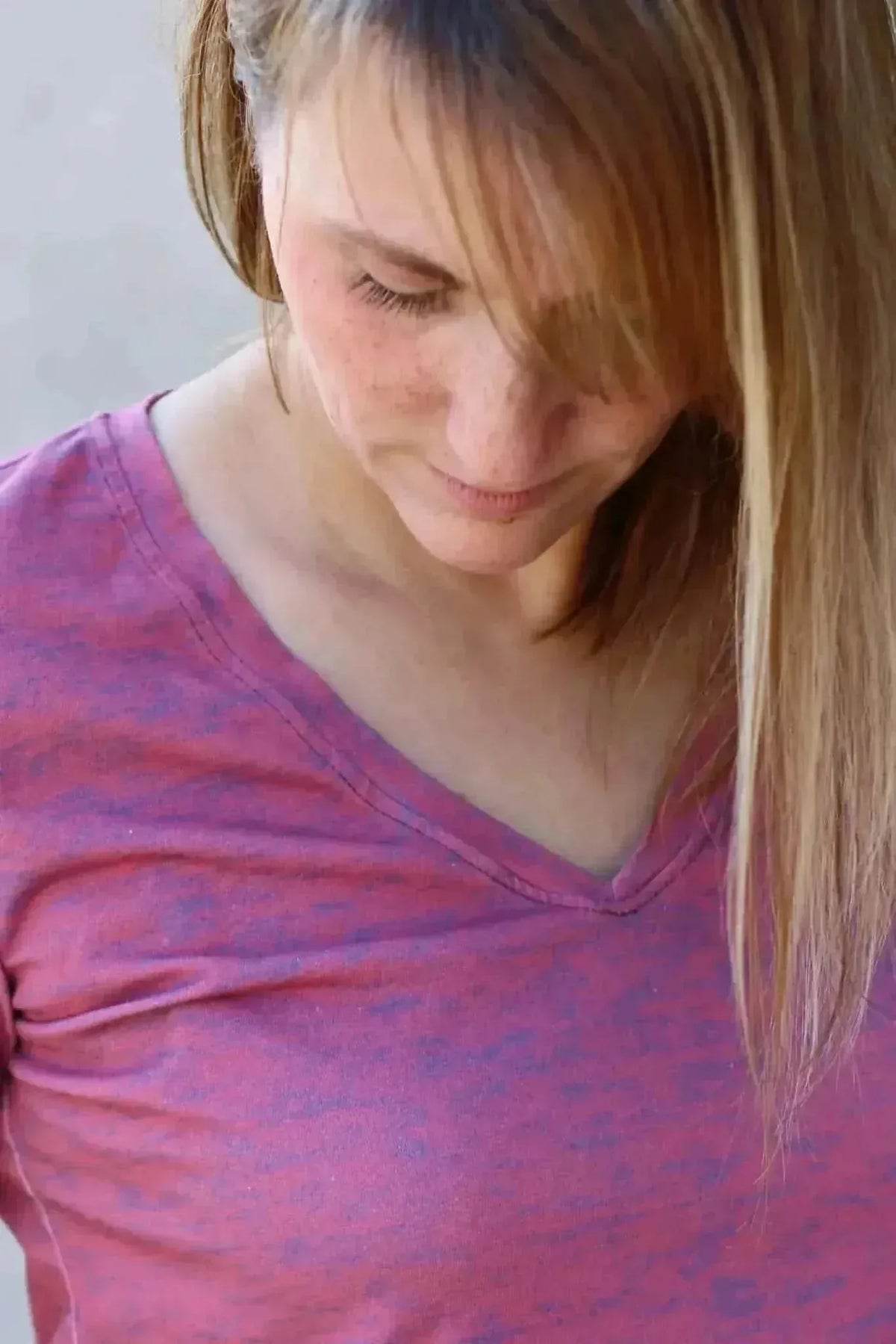 A woman in a red and purple heathered v-neck shirt looks down.