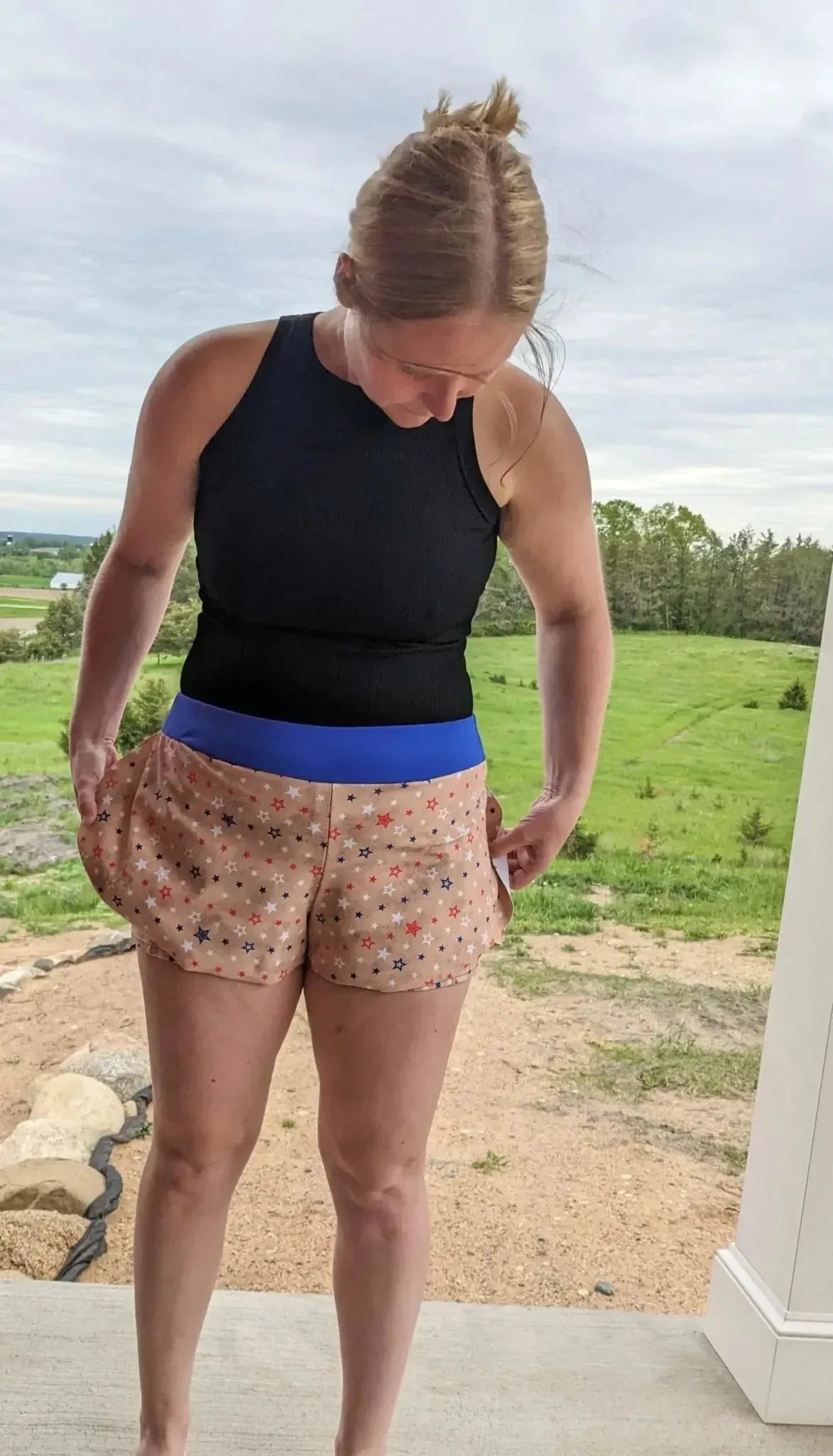 Woman wearing black tank top and orange star-patterned stretch shorts outdoors.