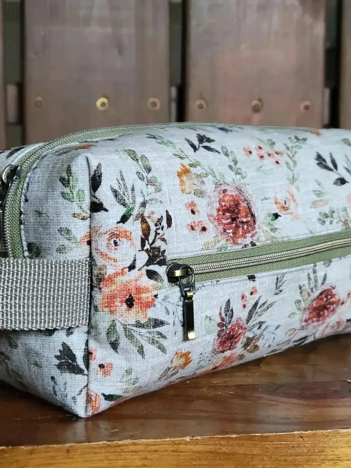 Rectangular zipper pouch with white floral fabric, green trim, and gray strap.