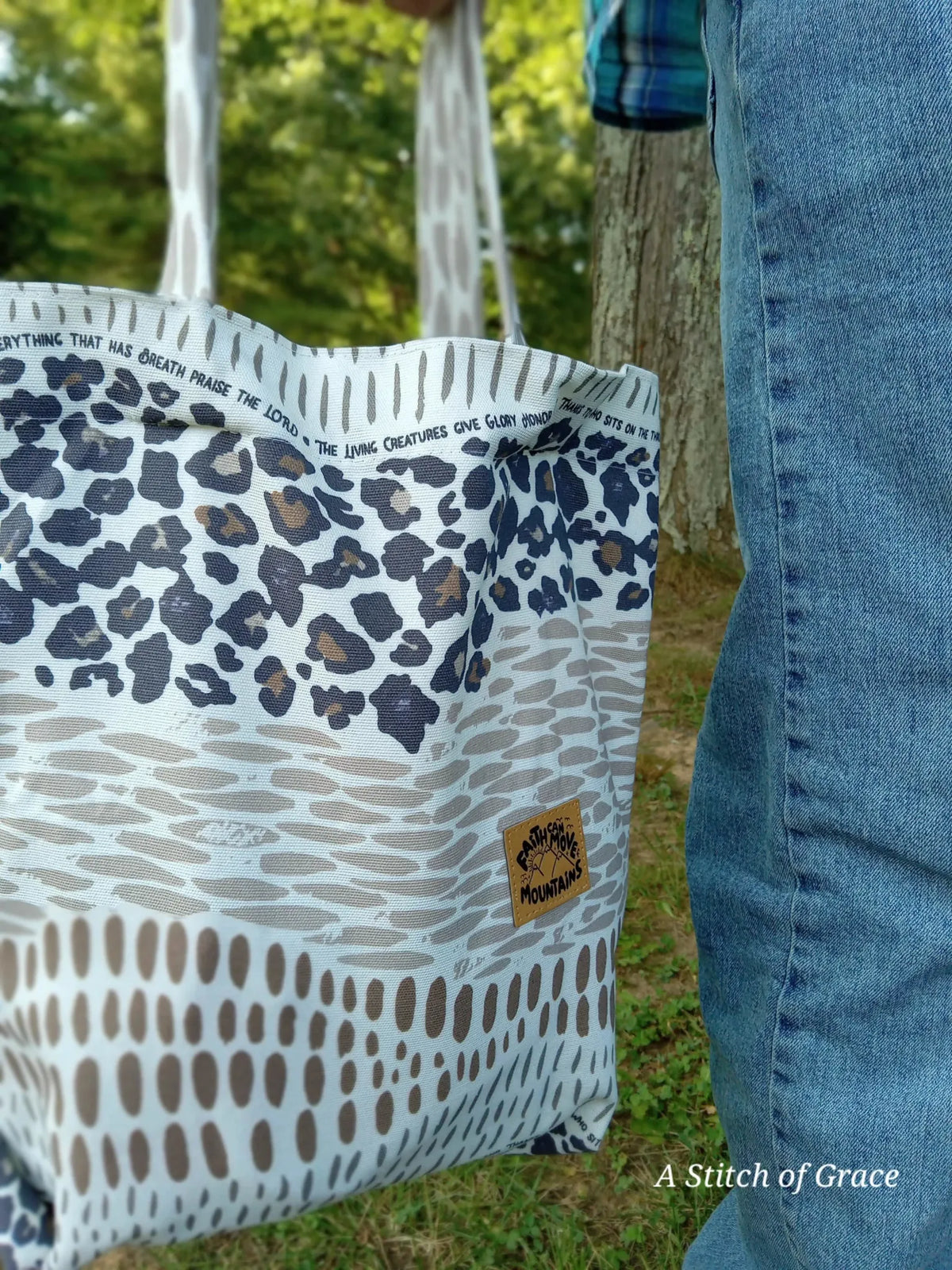A person holds a tote bag with leopard print and text, next to blue jeans.