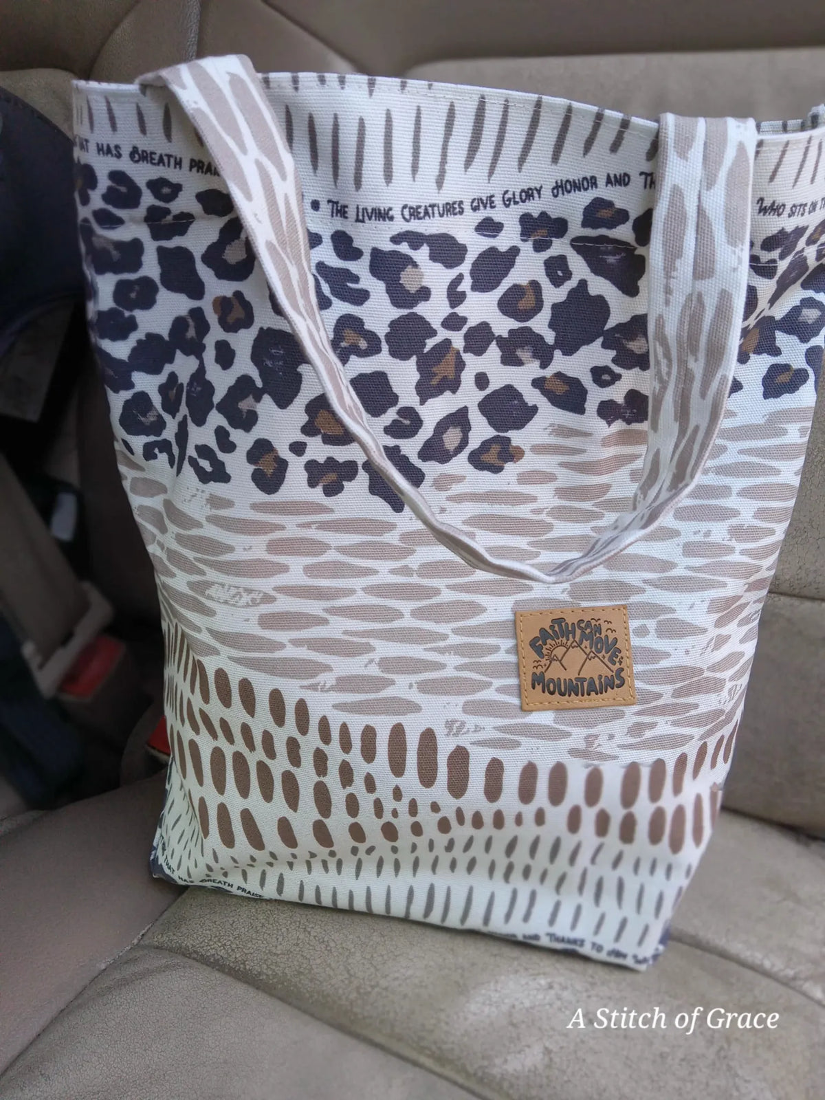 A tote bag with leopard print and text, sitting on a car seat.