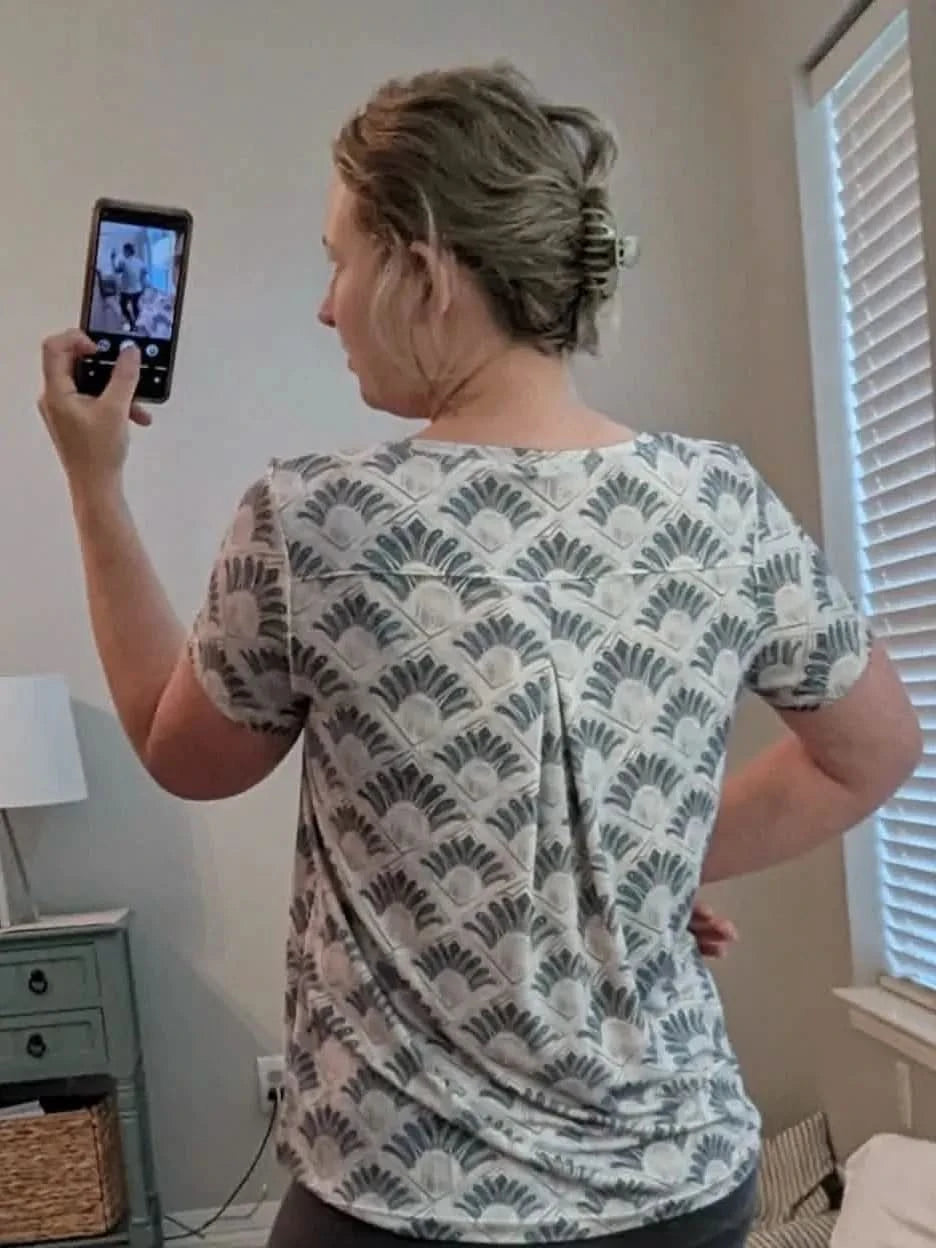A woman from behind wears a white and blue patterned short-sleeved shirt.