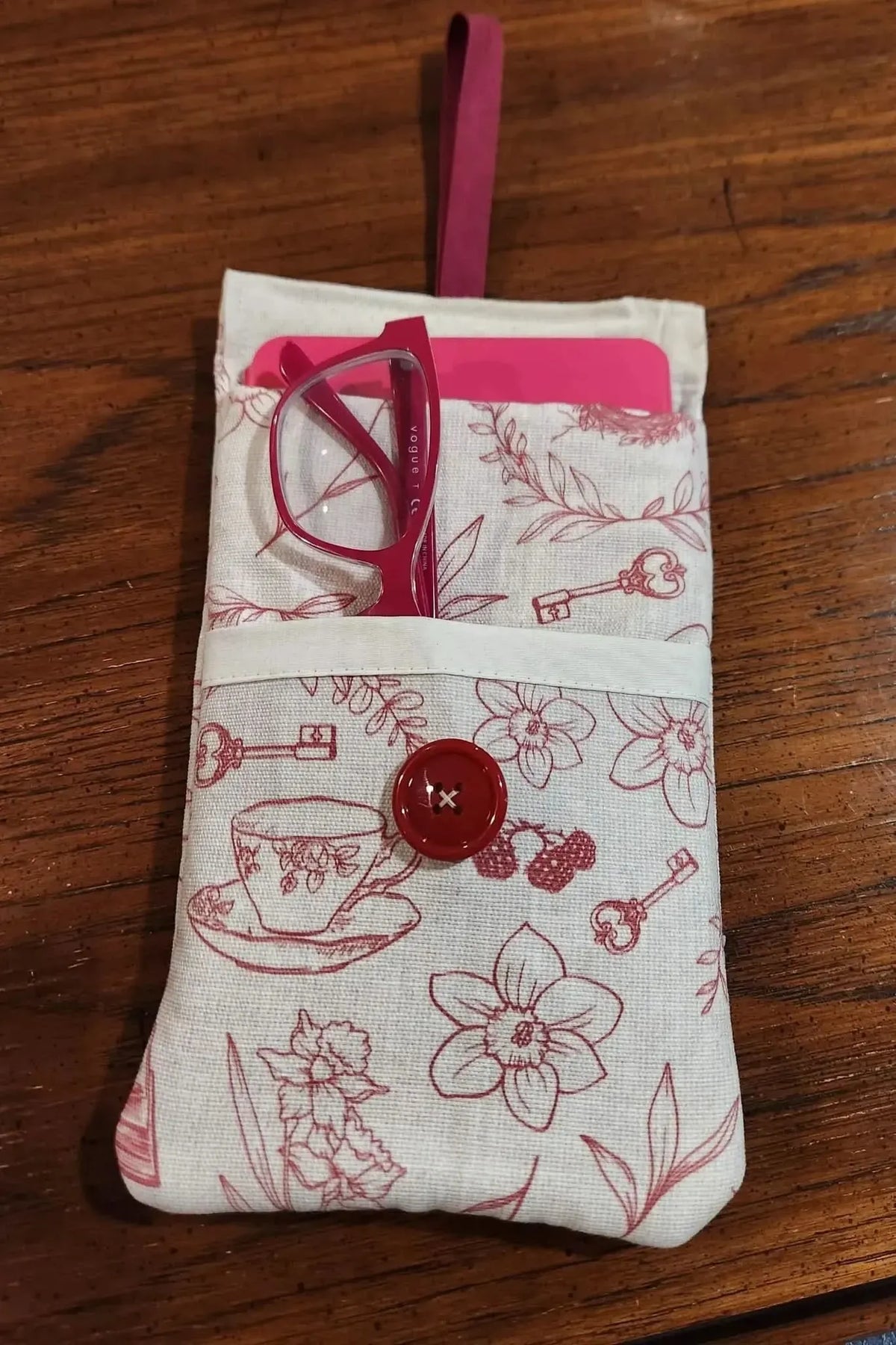 A fabric pouch with red tea, keys, and floral patterns, holding pink glasses and a phone.