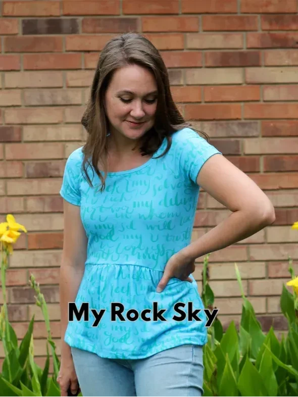 A woman models a light blue jersey top with a peplum hem and subtle text pattern.