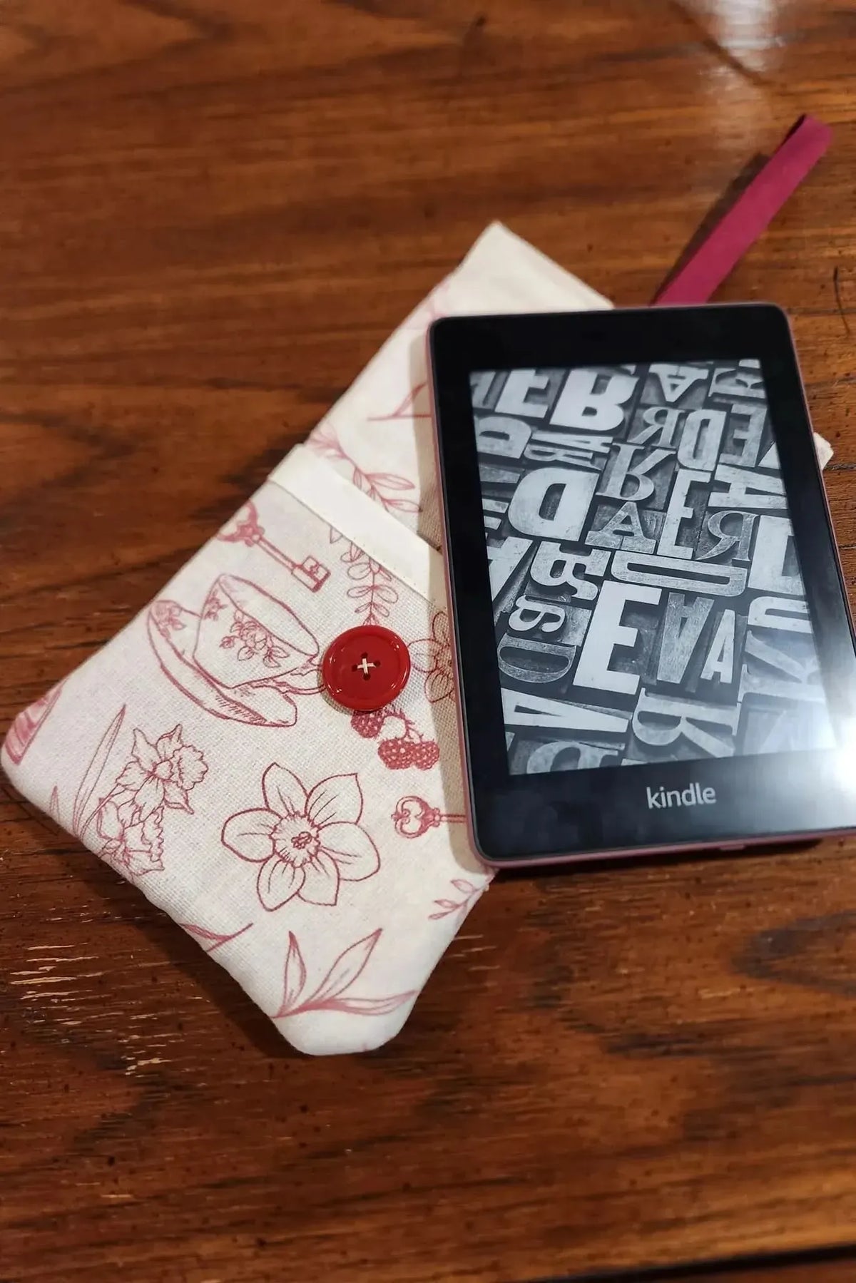 A Kindle and a fabric pouch with a red button and a tea and toile pattern.