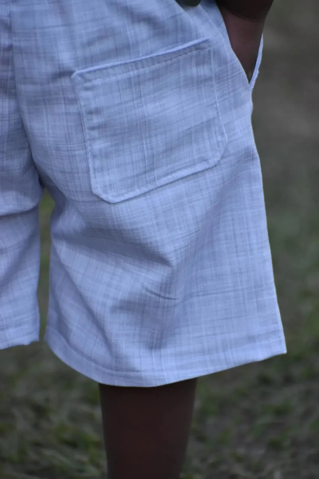 A person wears light blue shorts with a subtle plaid pattern and a back pocket.
