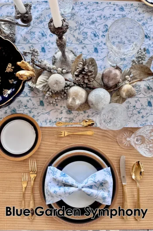 A table set with blue and white floral fabric, gold flatware, and a festive centerpiece.