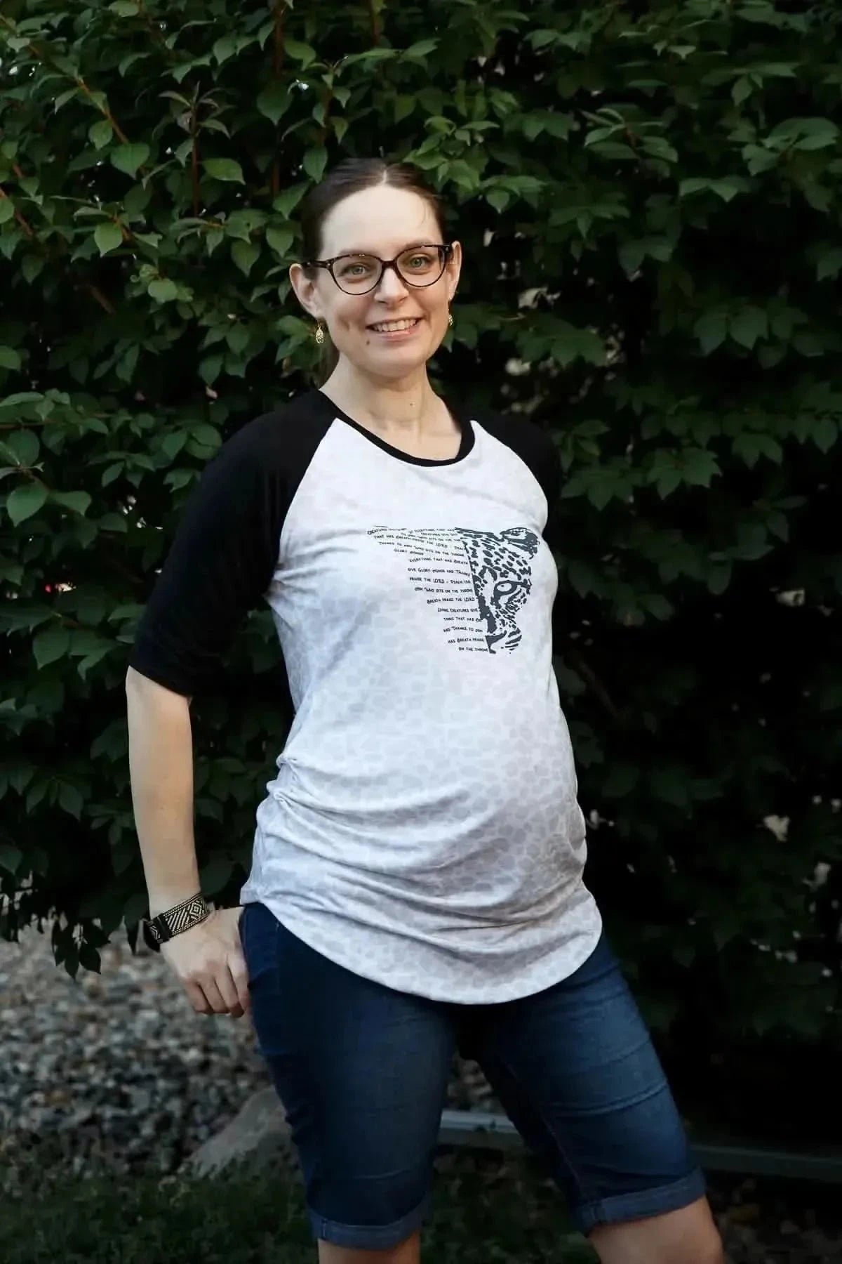 Pregnant woman wearing a white raglan T-shirt with black sleeves and Creatures Give Glory panel print.