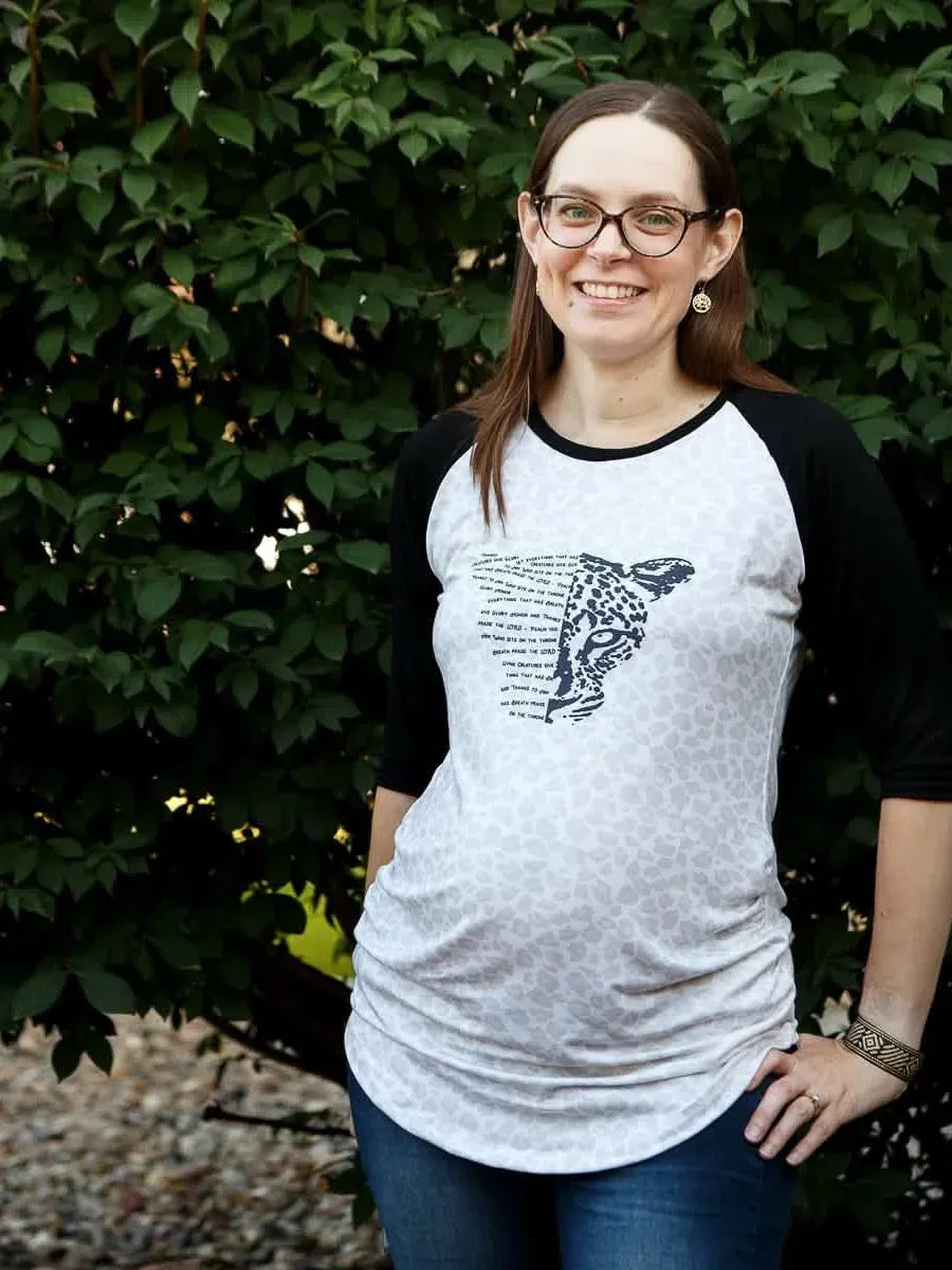 A woman smiles wearing a white and black raglan shirt with a leopard print and text.