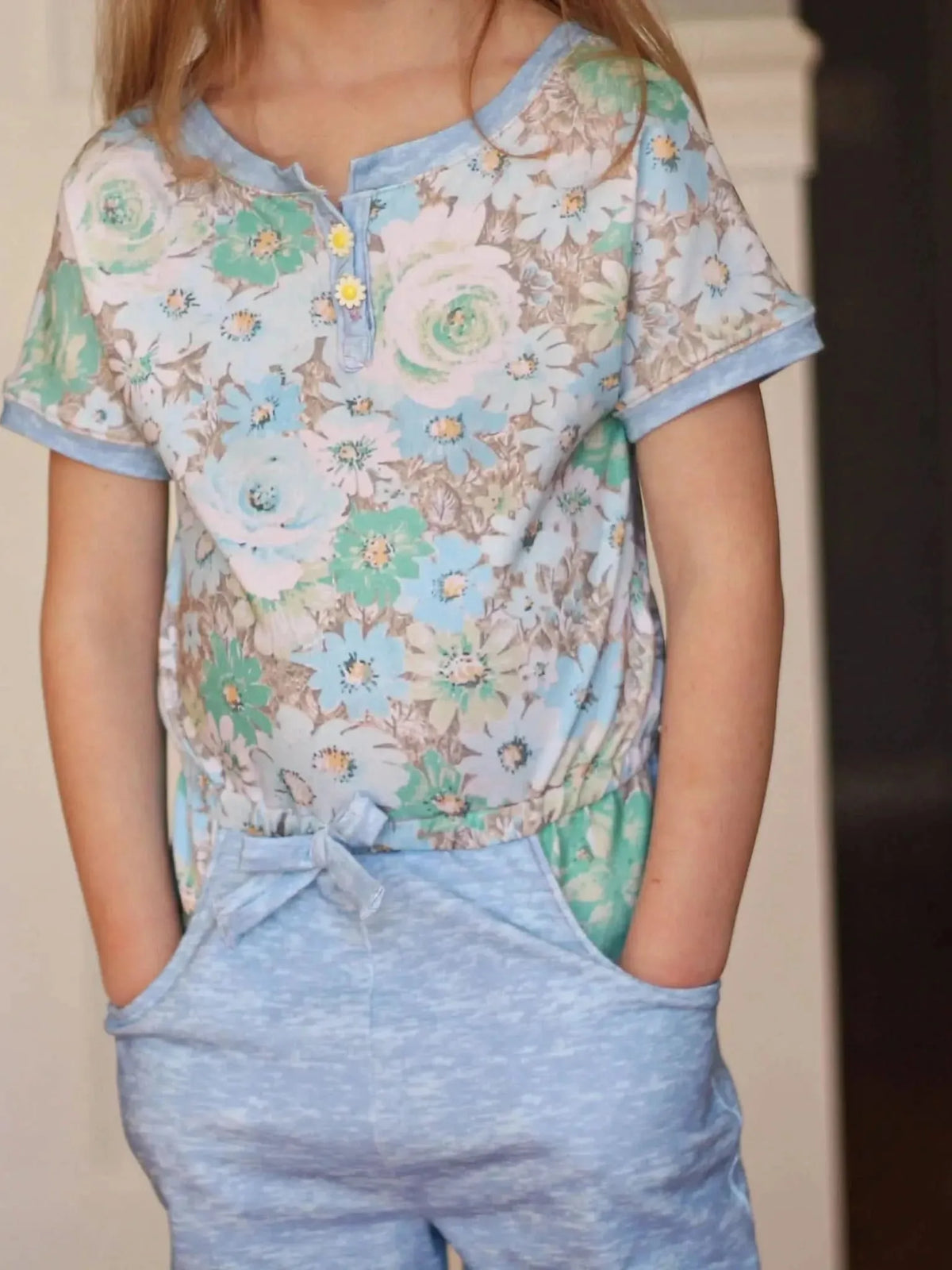A child models a floral print top with light blue pants.