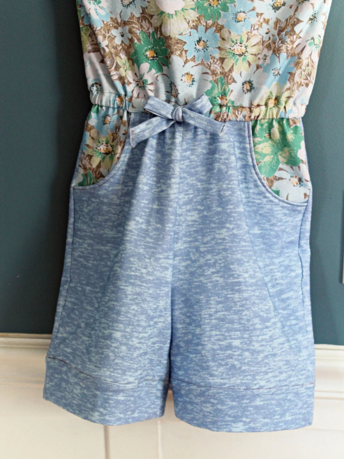 Light blue heather romper with a floral top and tie-front waist.