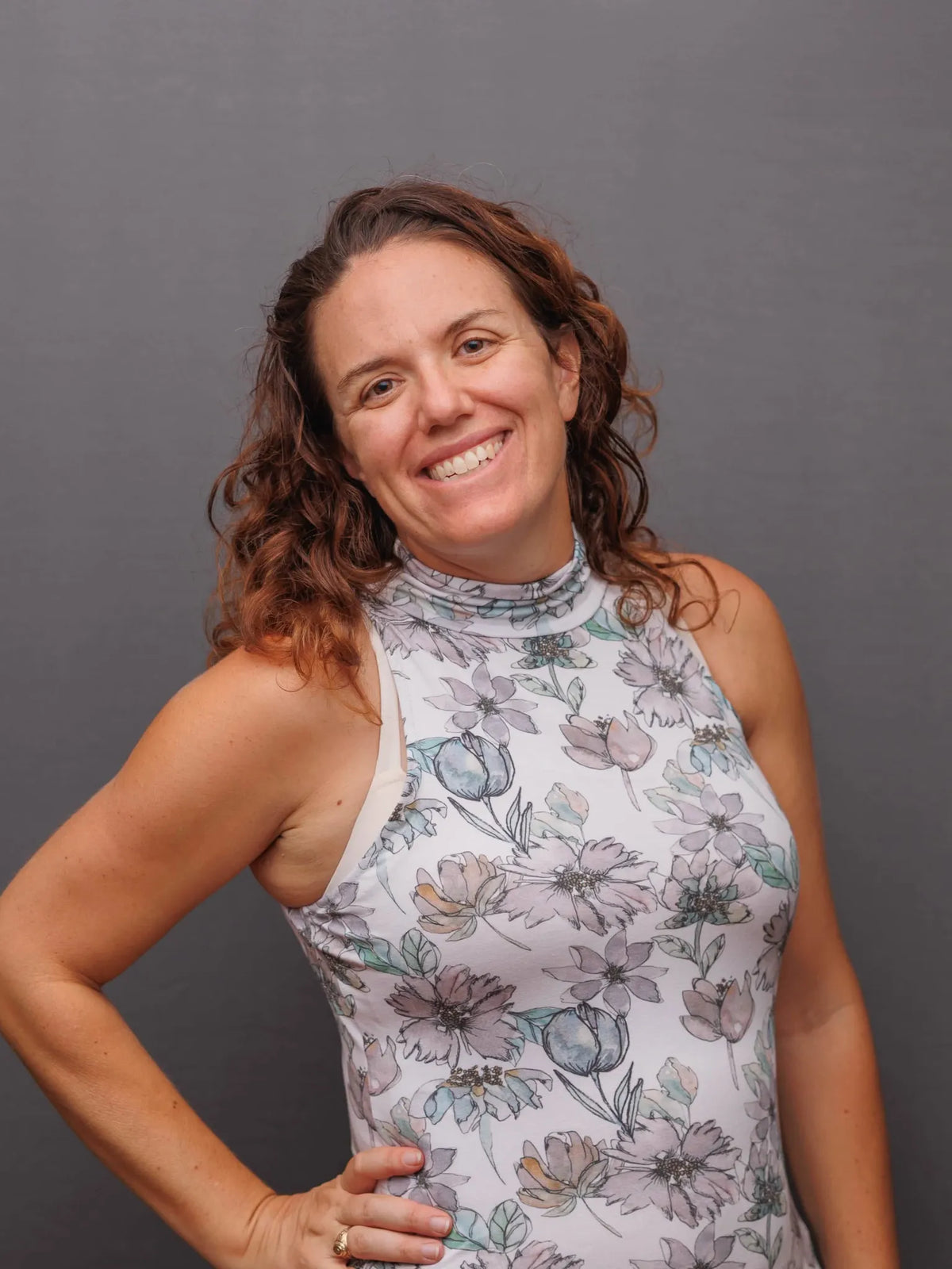 A woman in a floral top stands against a solid grey background.