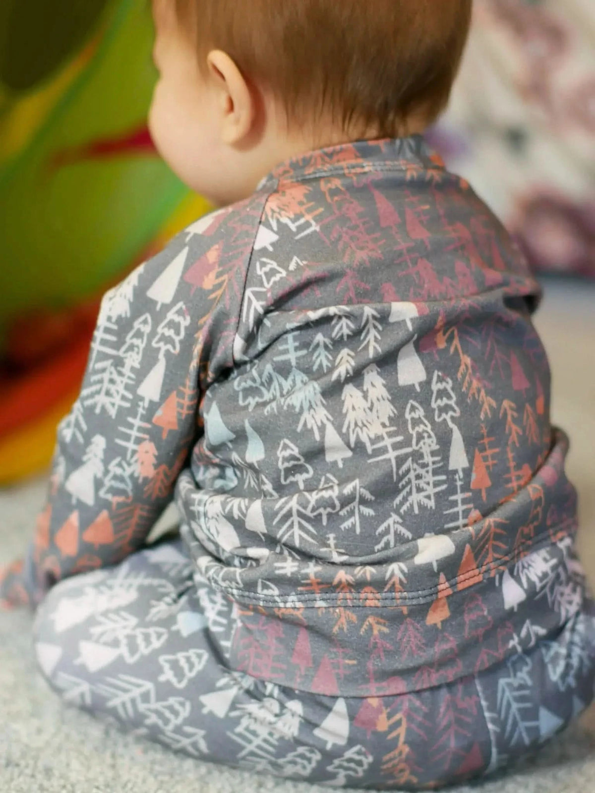 Baby in a dark fall trees patterned outfit, seen from behind.