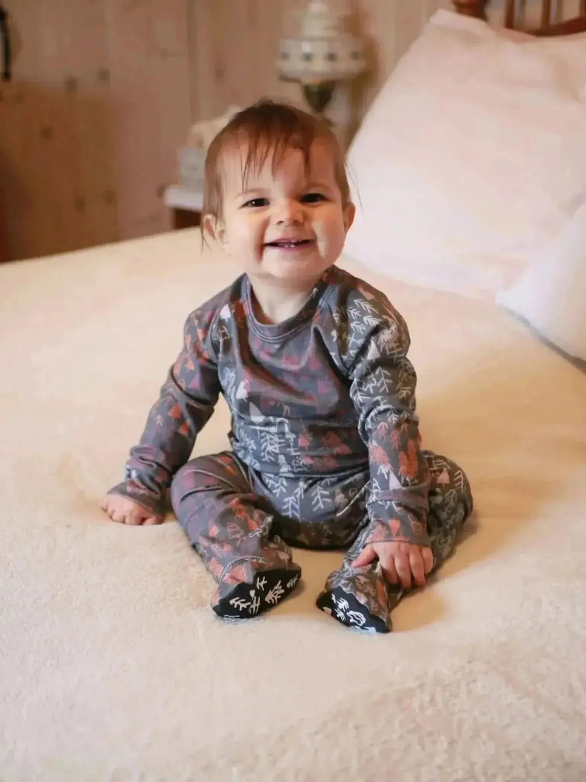 Baby wearing pajamas with a dark fall trees woodland fabric print.