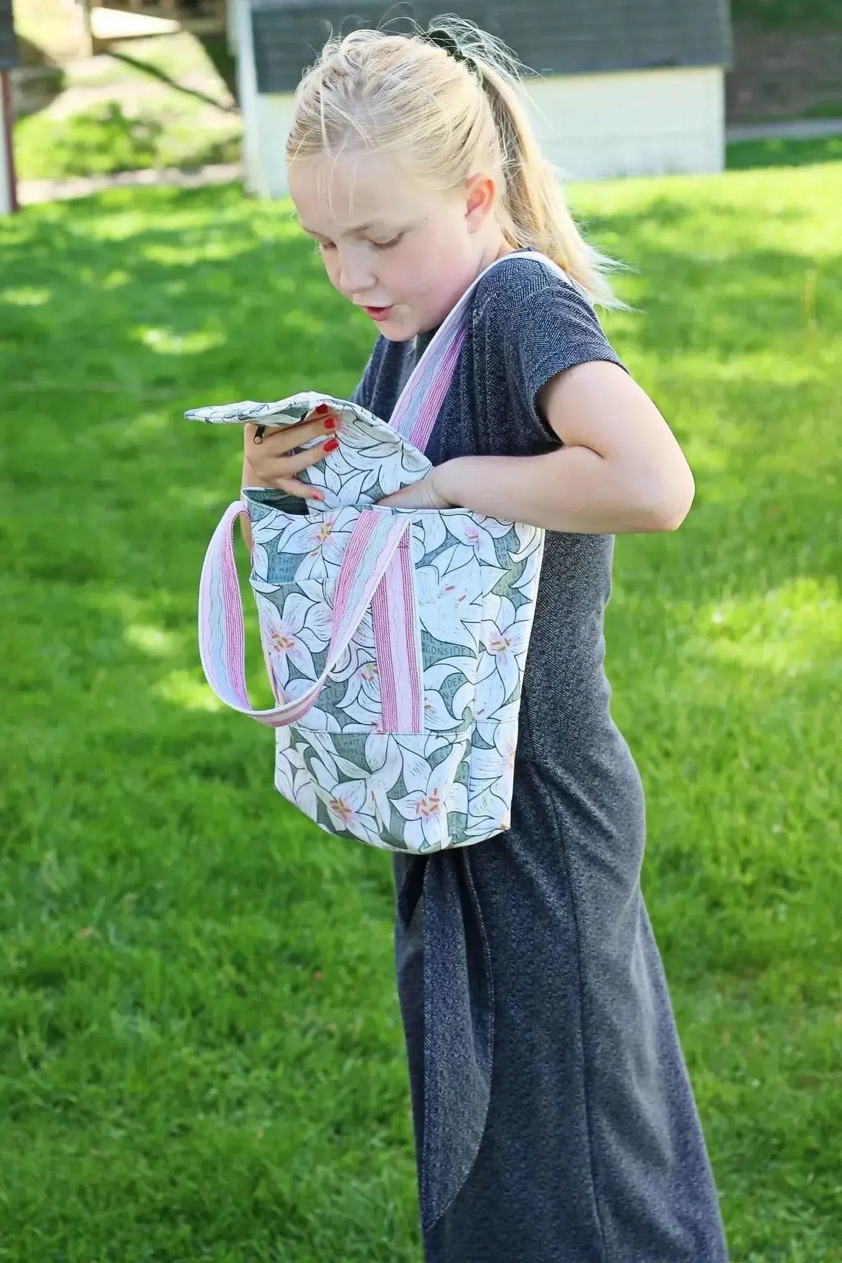 Lilies in green botanical print fabric sewn into an open tote bag carried by a girl outdoors.
