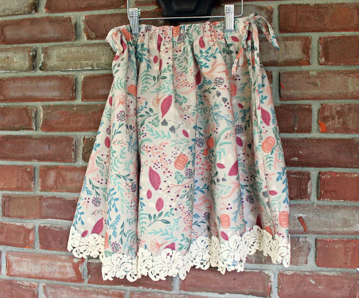 A tan skirt with a colorful forest foliage pattern and lace trim hangs on a brick wall.