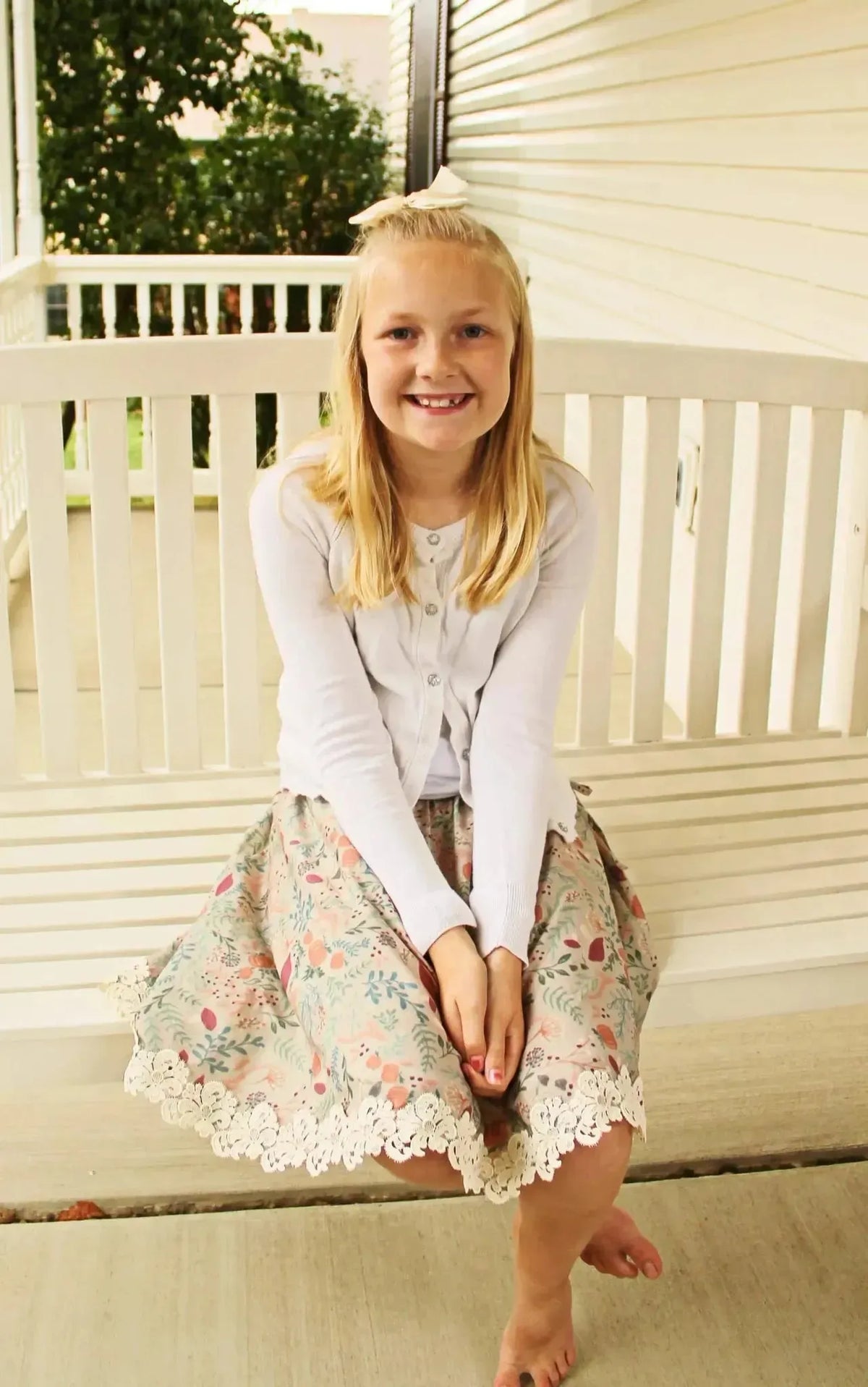Tan botanical fabric with forest foliage print, shown as a girl's skirt on a porch bench.