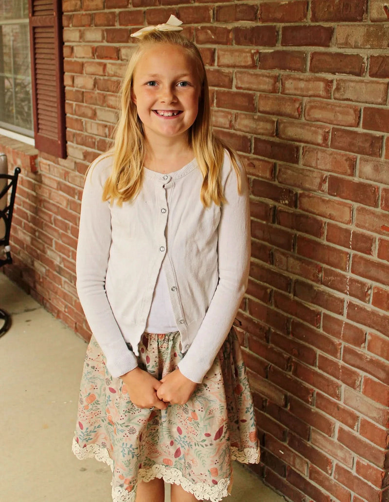 A young girl wears a tan skirt with a forest foliage pattern.
