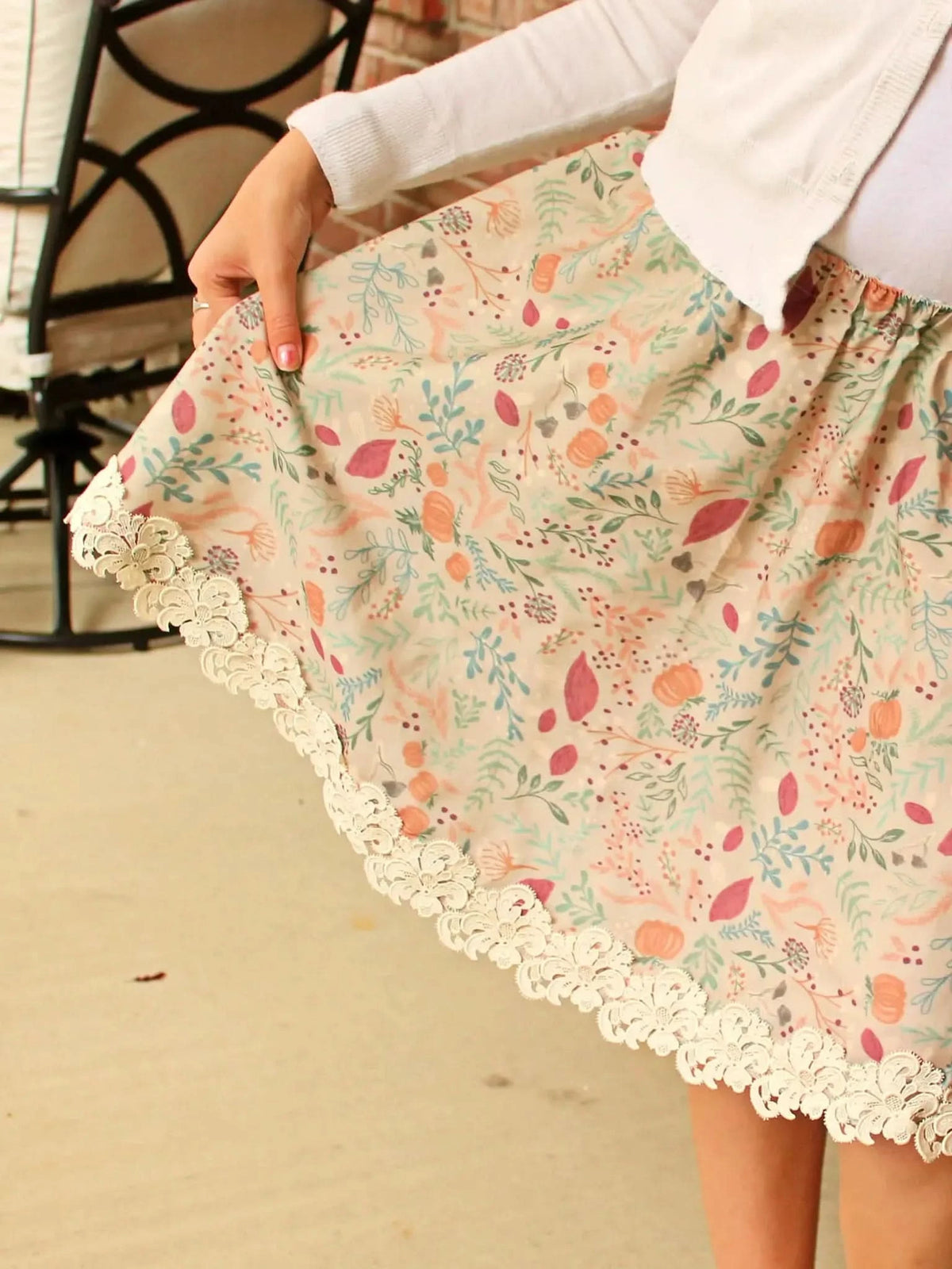 A person wears a tan skirt with a forest foliage pattern and lace trim.