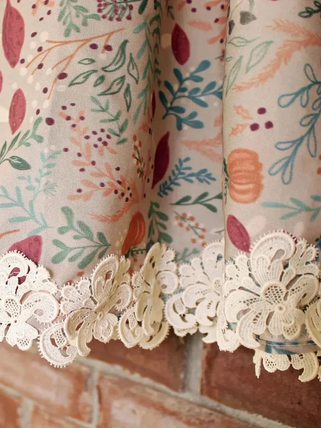 Forest Foliage in Tan fabric with lace trim against a brick wall.