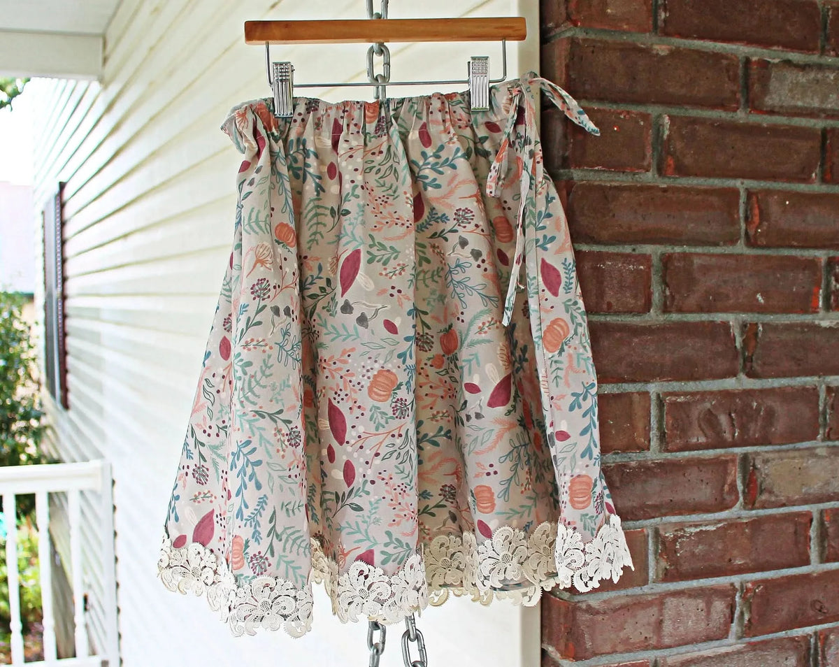 A tan skirt with a forest foliage pattern and lace trim hangs on a hanger.