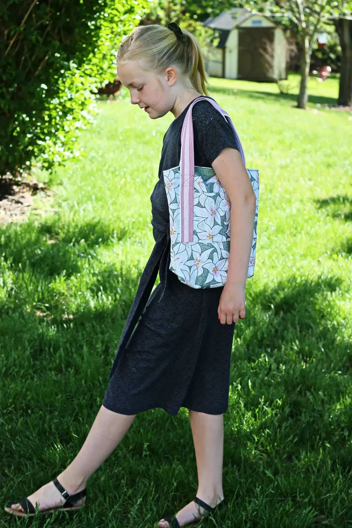 A girl carries a tote bag with a white lily and green leaf pattern.