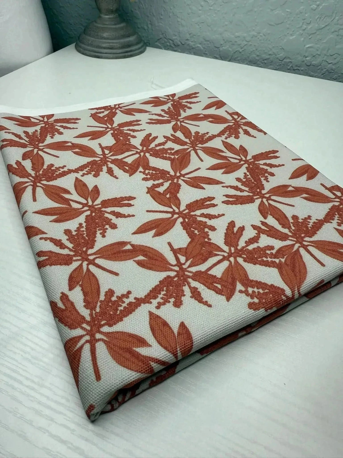 Folded fabric with pink autumn leaves print on a white table.