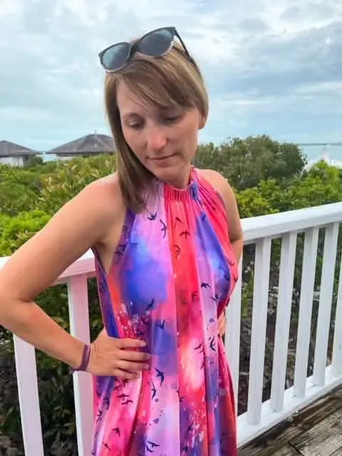 A woman wears a vibrant purple and pink dress with a bird pattern.