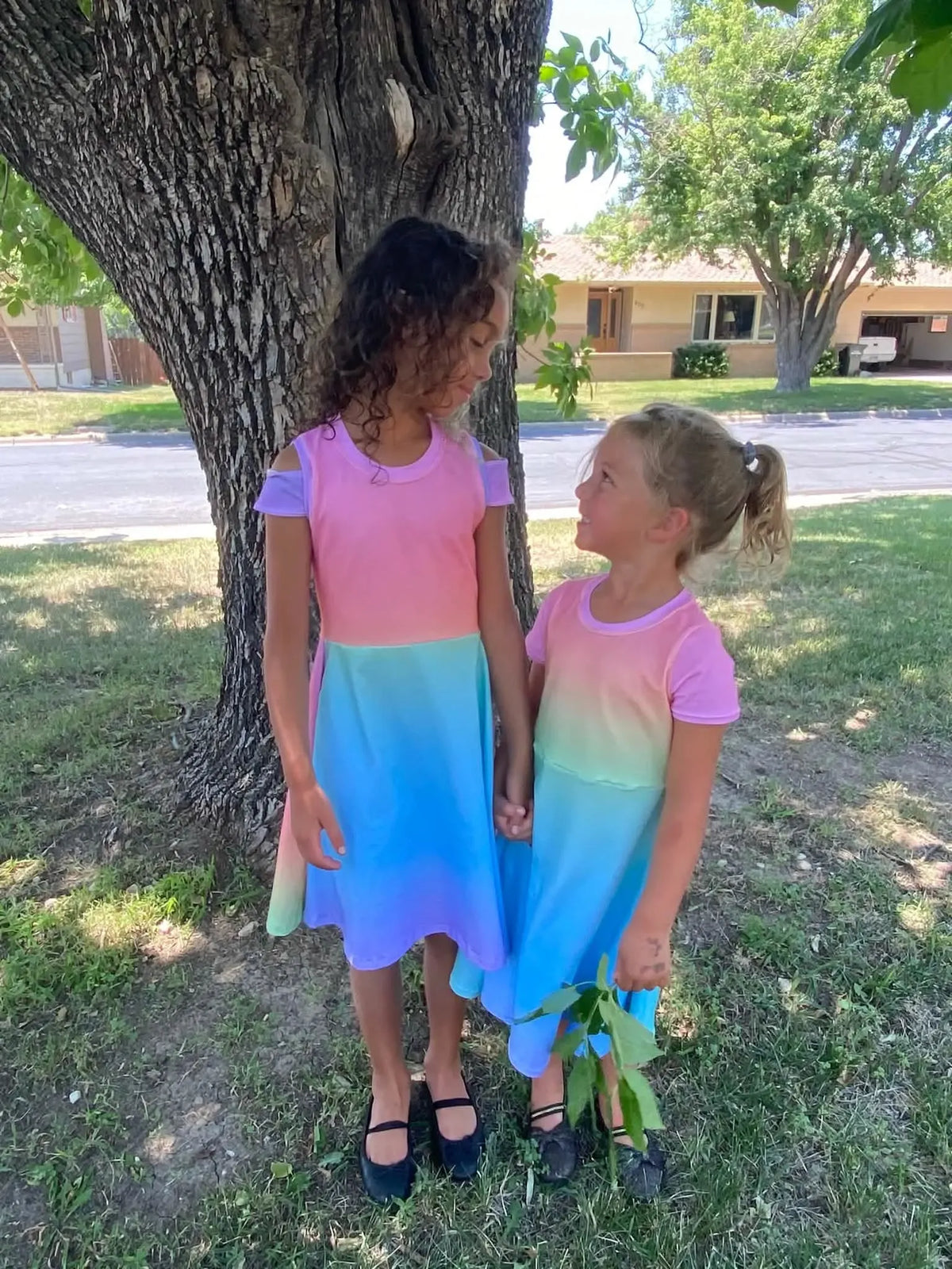 Two girls wear matching ombre dresses in pink, purple, blue, and green.