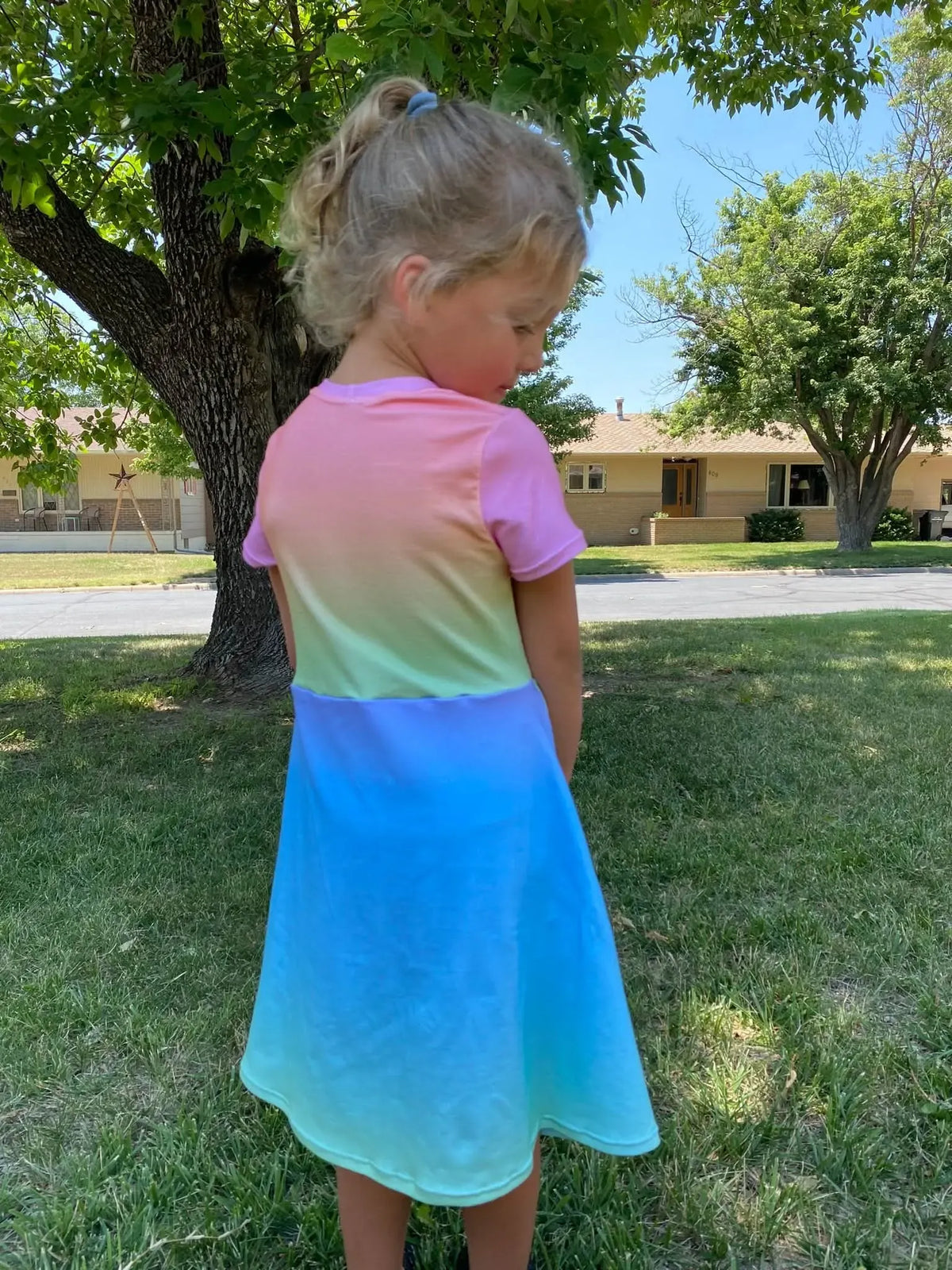 A young girl wears a colorful ombre dress, standing with her back to the camera.