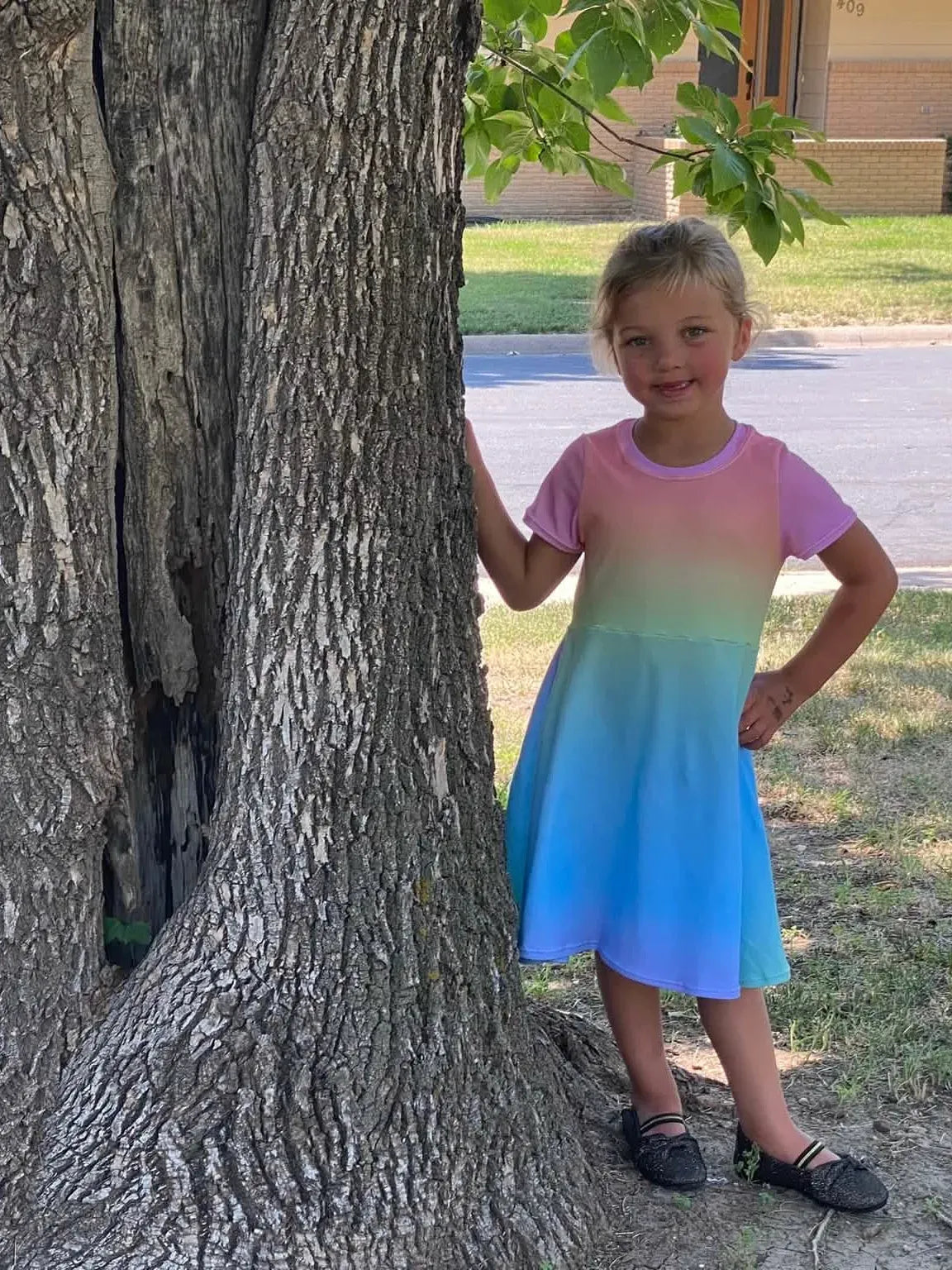 Two girls in ombre dresses stand by a tree.