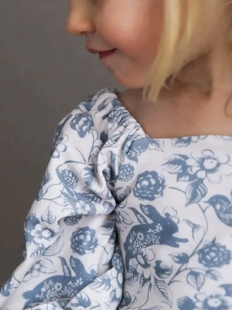 A child in a blue and white floral top with bunnies and birds.