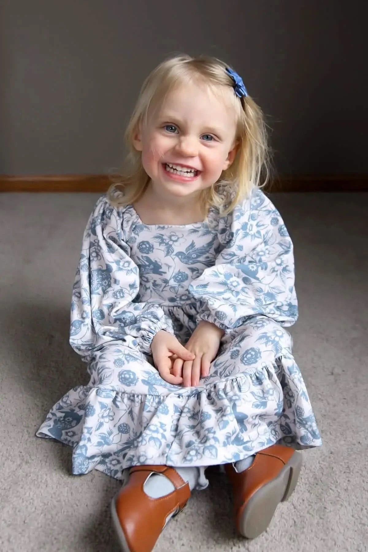 A young girl in a blue and white floral dress with birds and berries.