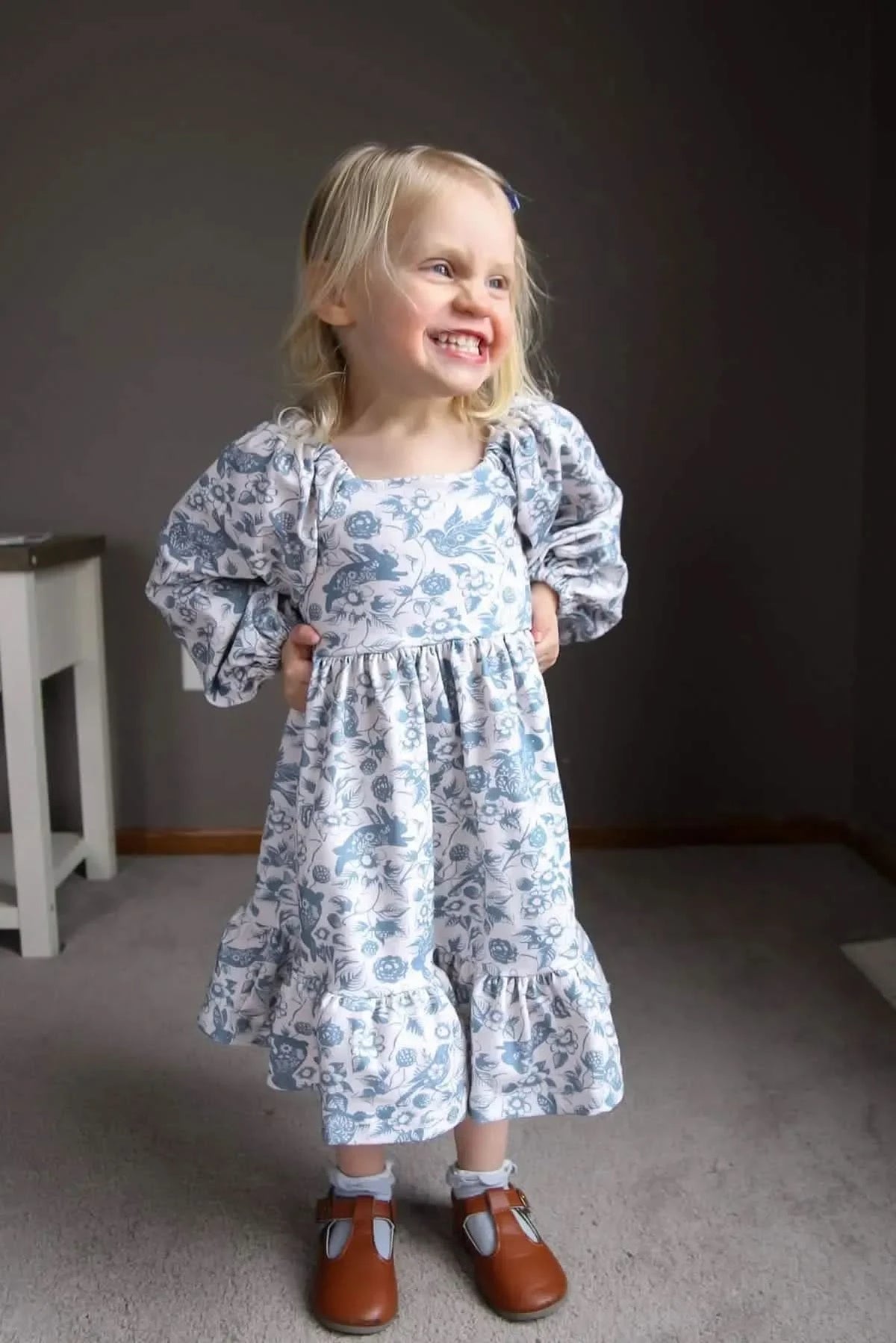 A young girl in a blue and white floral dress with bunny and bird patterns.