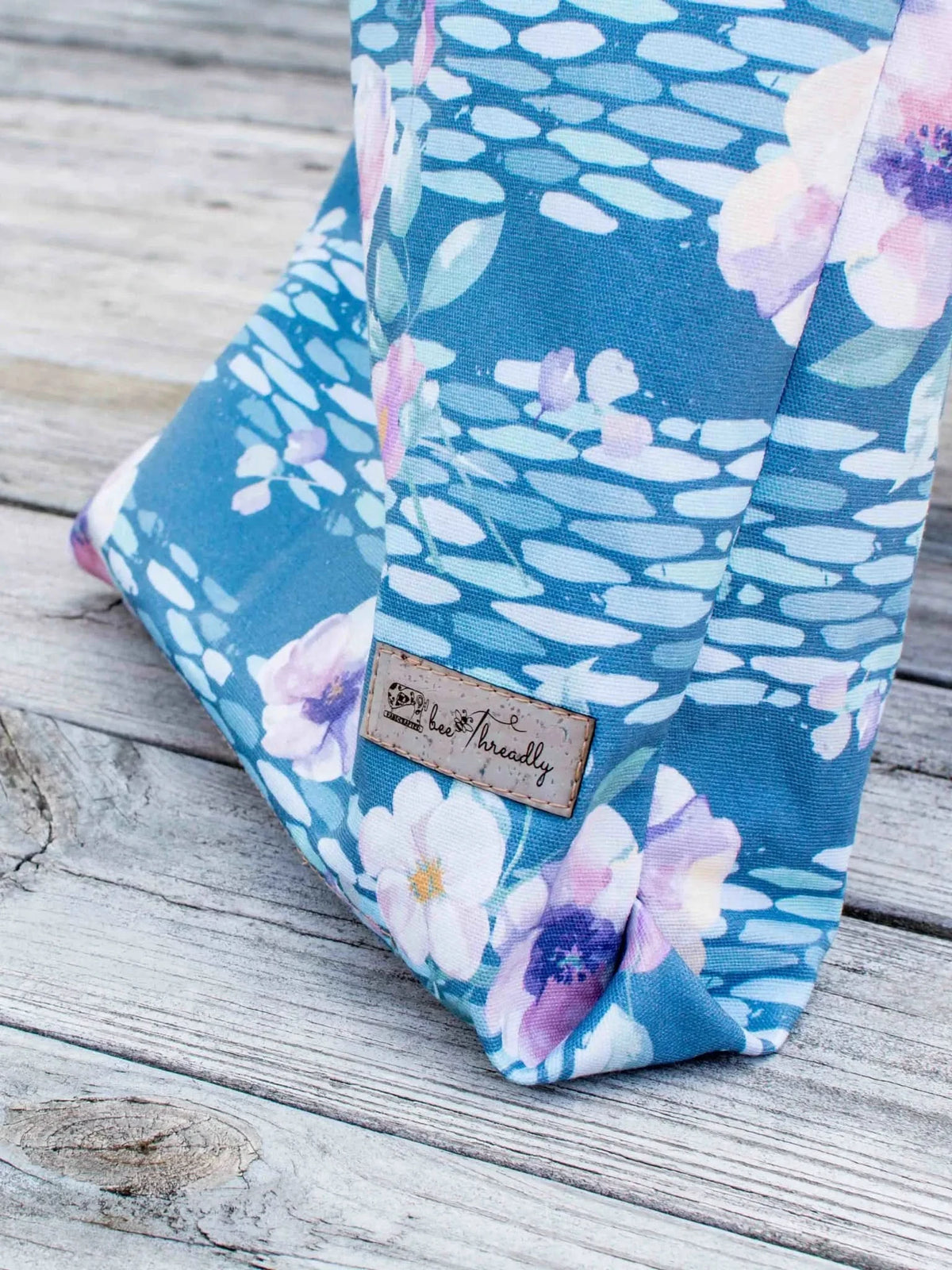 A blue fabric with a watercolor floral pattern and a "bee threadly" label.