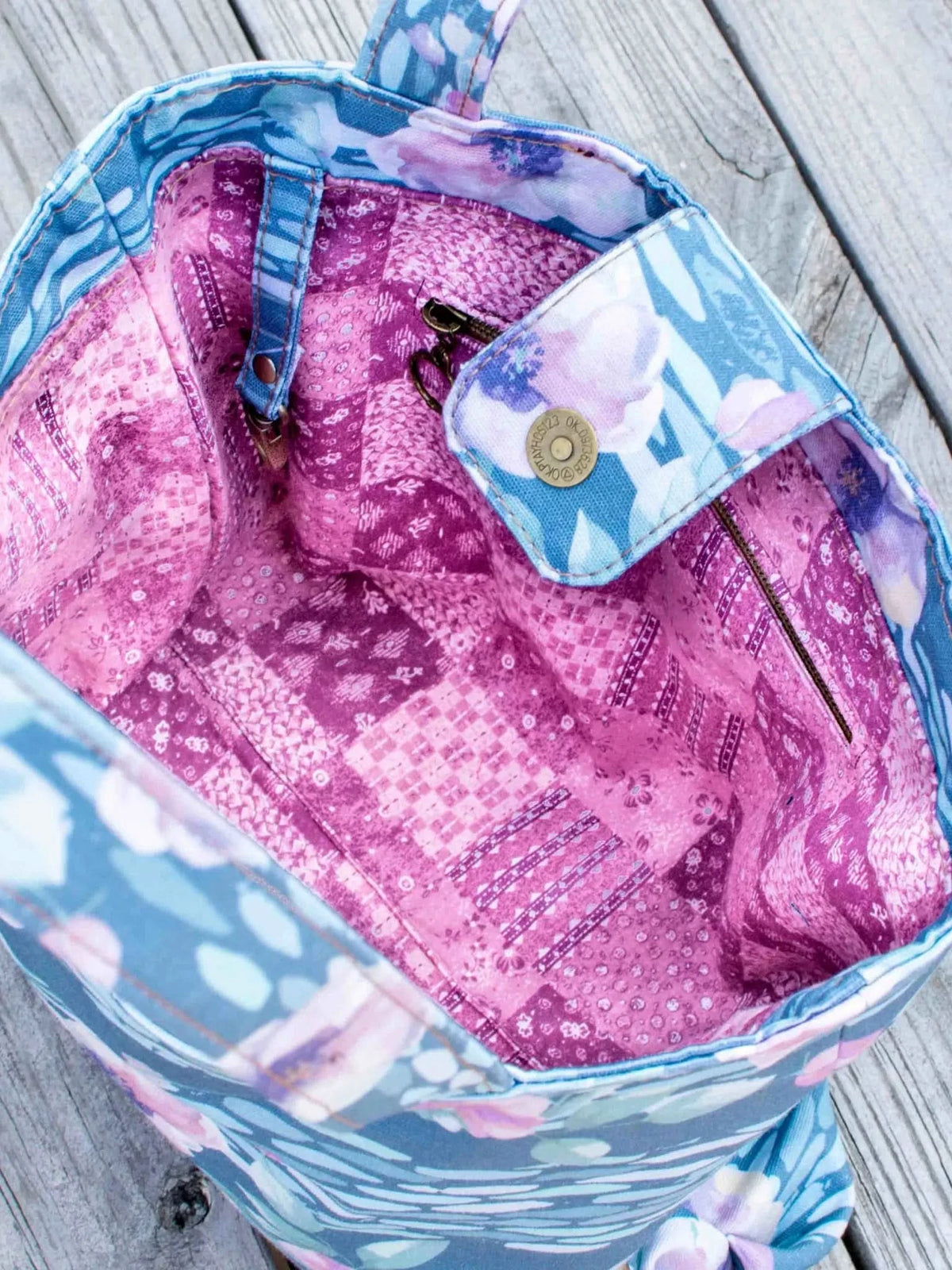 A floral tote bag with a pink and purple patterned lining sits on a wooden surface.