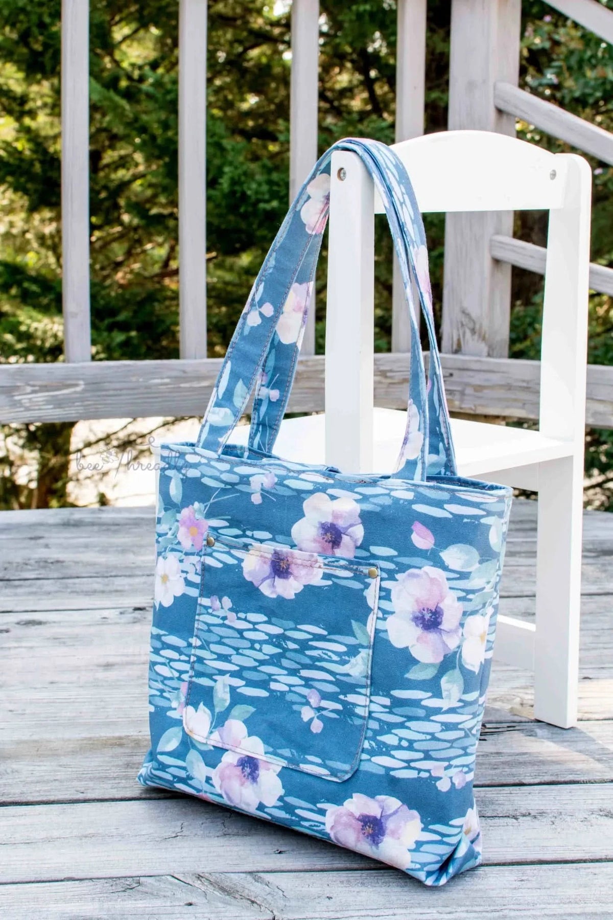 A blue floral tote bag with a front pocket hangs on a white chair.