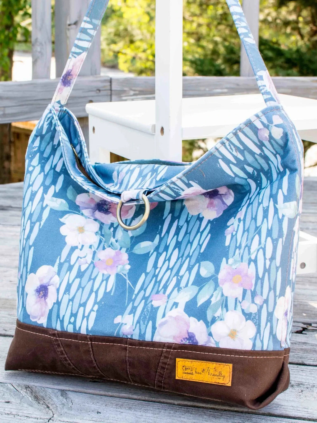 A blue floral bag with a brown base sits on a wooden deck.
