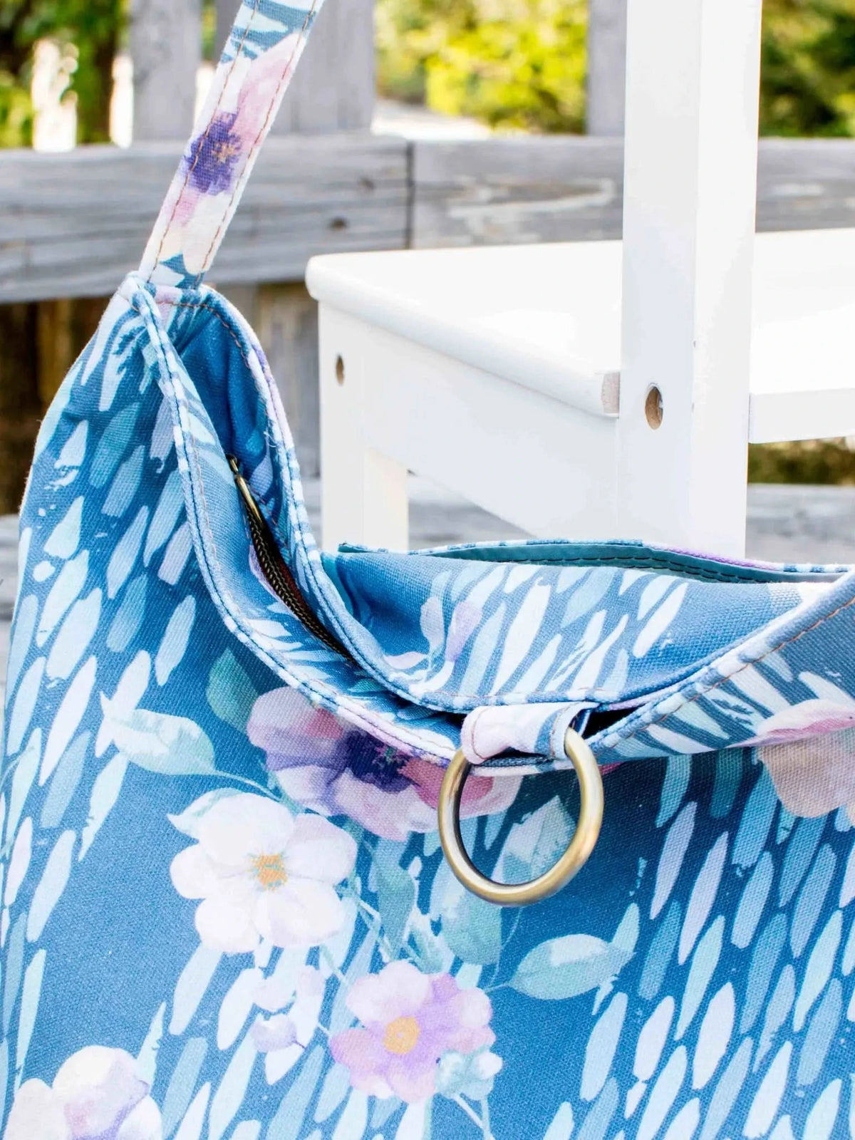 A blue floral fabric bag with a zipper and a gold ring is shown outdoors.