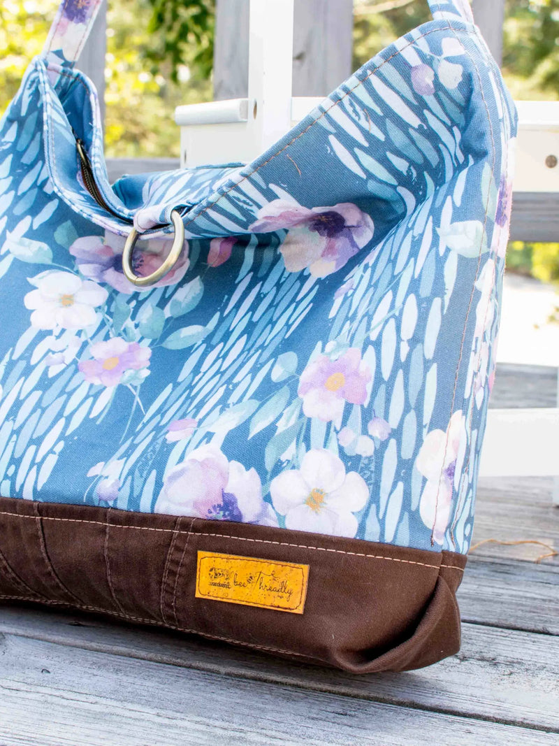 A blue floral bag with a brown base sits on a wooden deck.