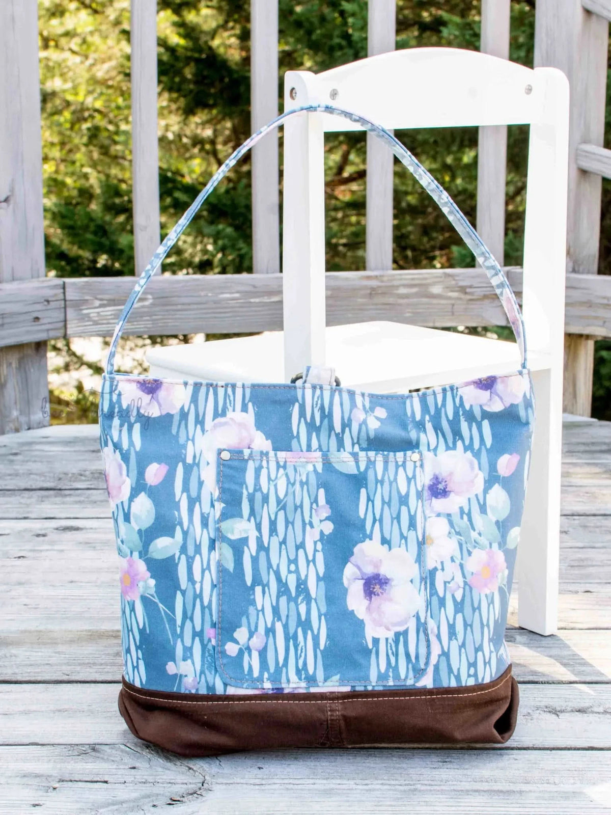 A blue floral tote bag with a brown base sits on a wooden deck.