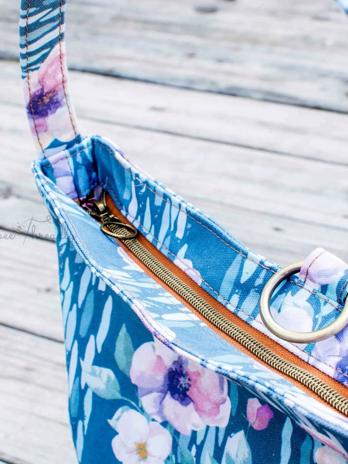 A blue floral fabric bag with a brown zipper and a metal ring.