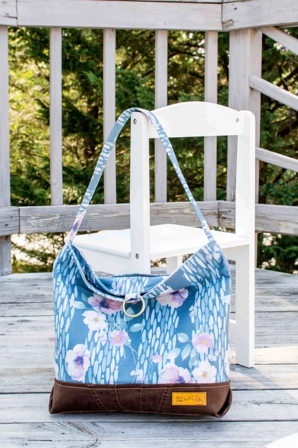 A blue floral tote bag with a brown base sits on a wooden deck.