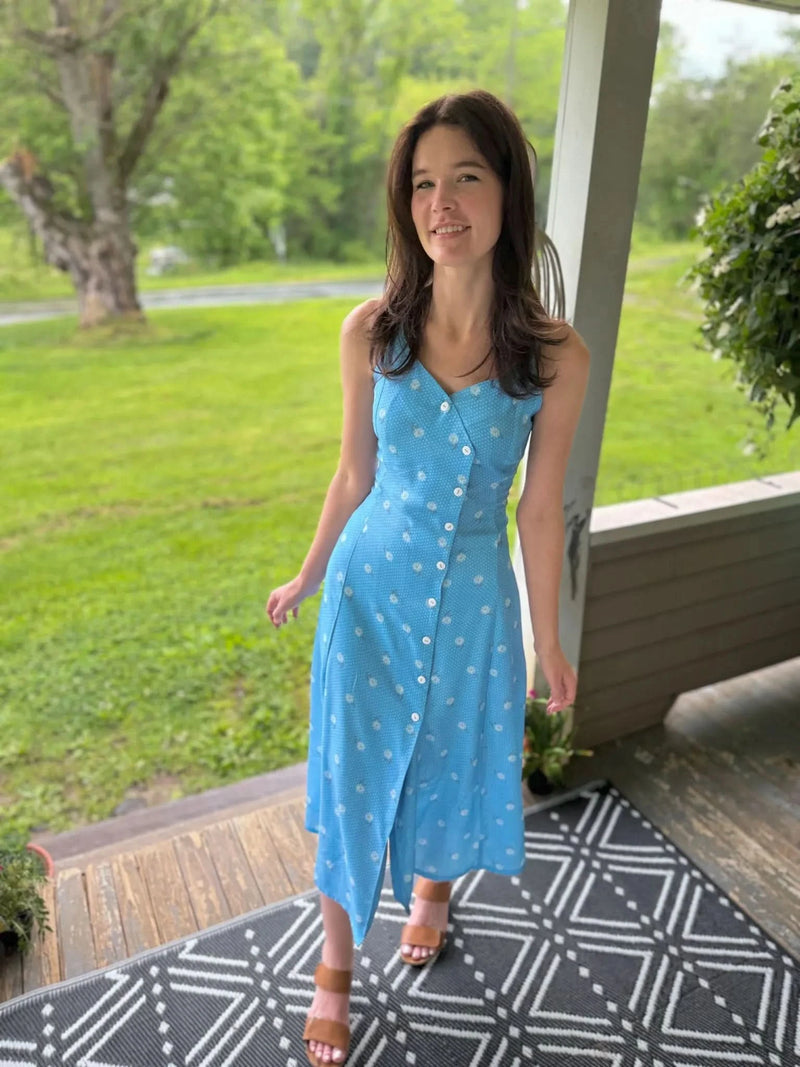 A woman in a blue dress with white floral patterns and brown sandals.