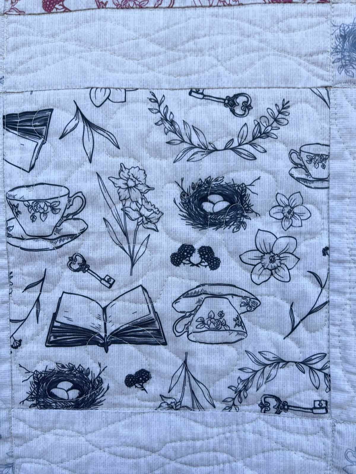 A white fabric with black sketches of teacups, keys, flowers, and nests.