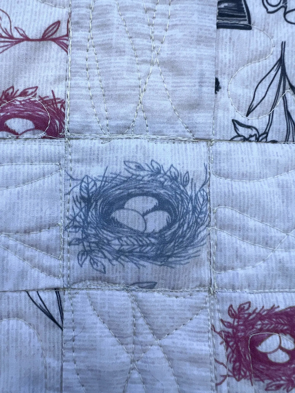 A quilted fabric features a blue bird's nest with three eggs, surrounded by other patterns.