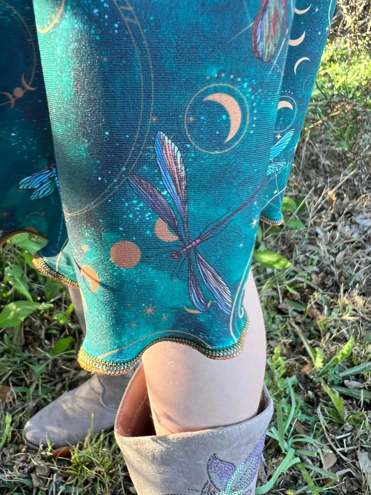 A person wears a teal dress with celestial dragonfly patterns and light brown boots.