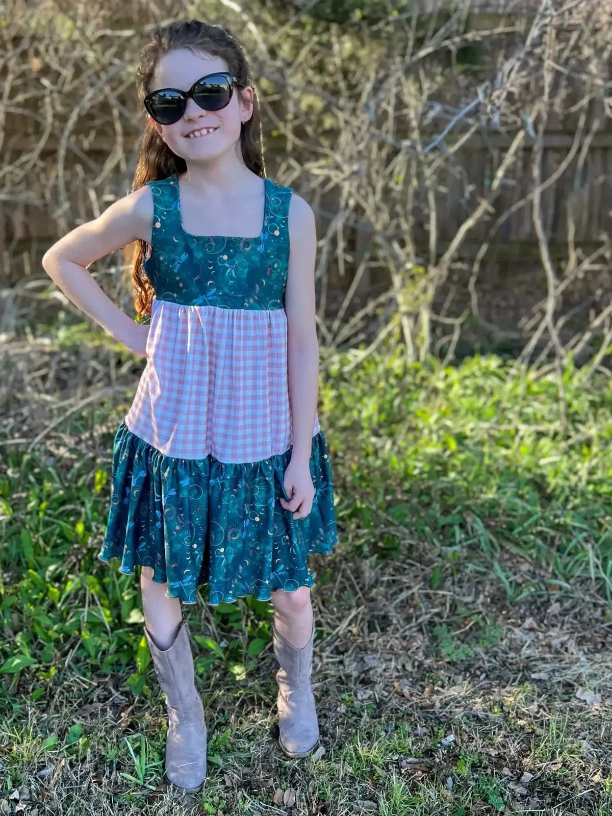 Girl in green and pink checkered dress with celestial dragonfly print, outdoors.