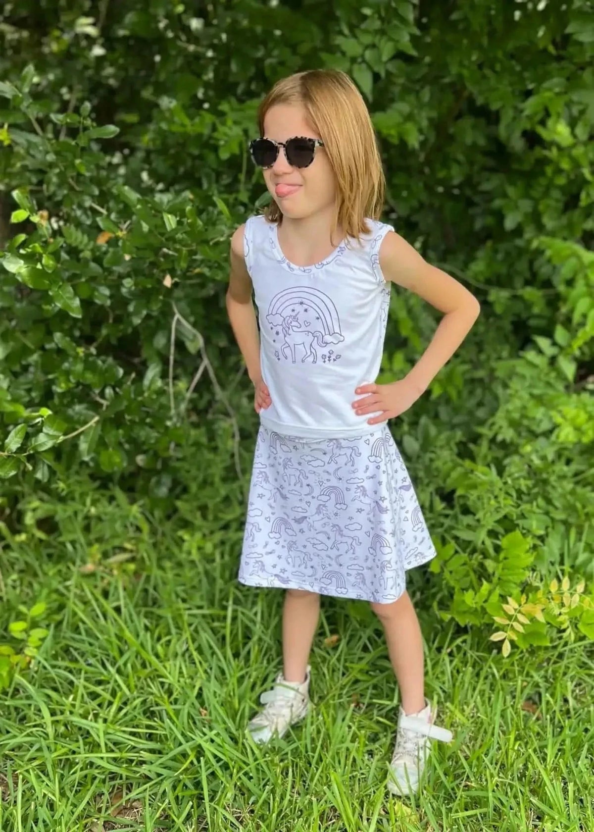 Girl in white unicorn-print tank top and purple skirt standing outdoors.